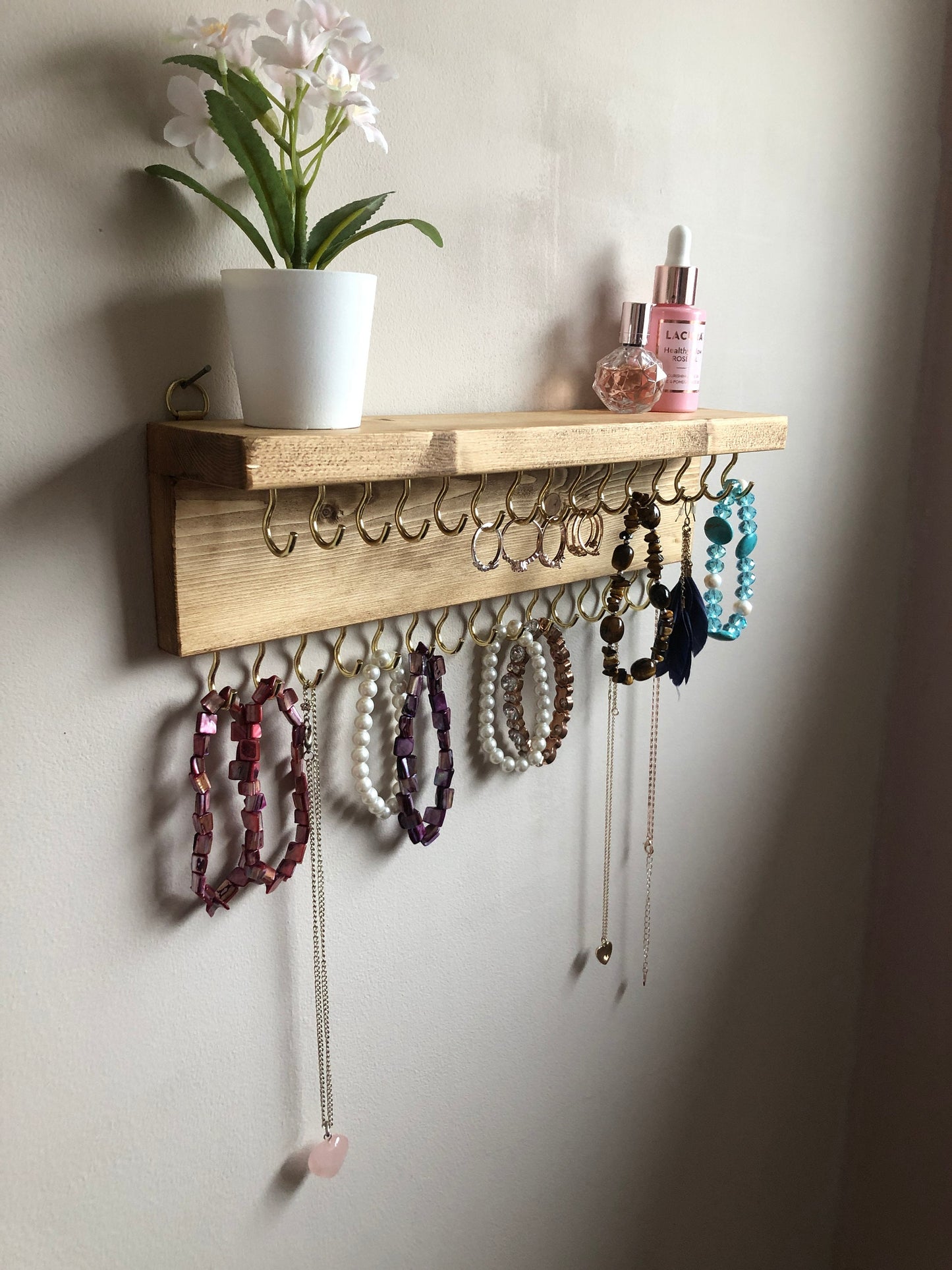 Wall-mounted jewellery organiser with 30 hooks, available in various colours including Woodland and Rustic Oak. Handcrafted from carefully selected timber, each piece boasts unique natural grain patterns. Customize with brass or upgrade to silver/chrome hooks and D rings
