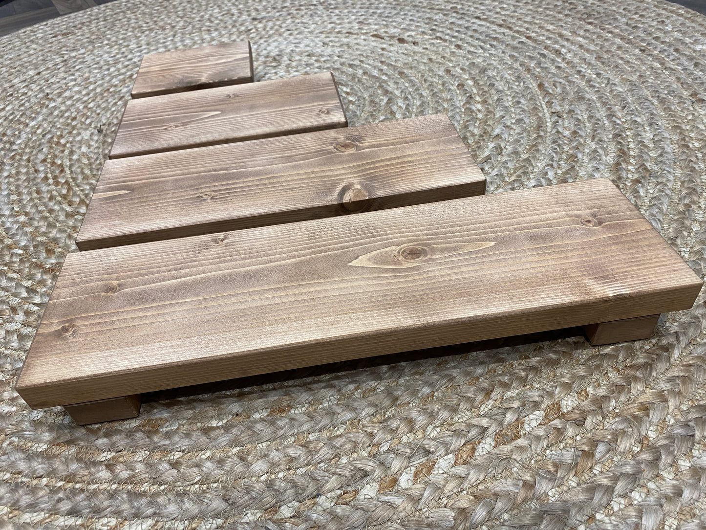 A wooden shelf that stands on two flat wooden legs. It is ideal for placing items on like bottles or candles.