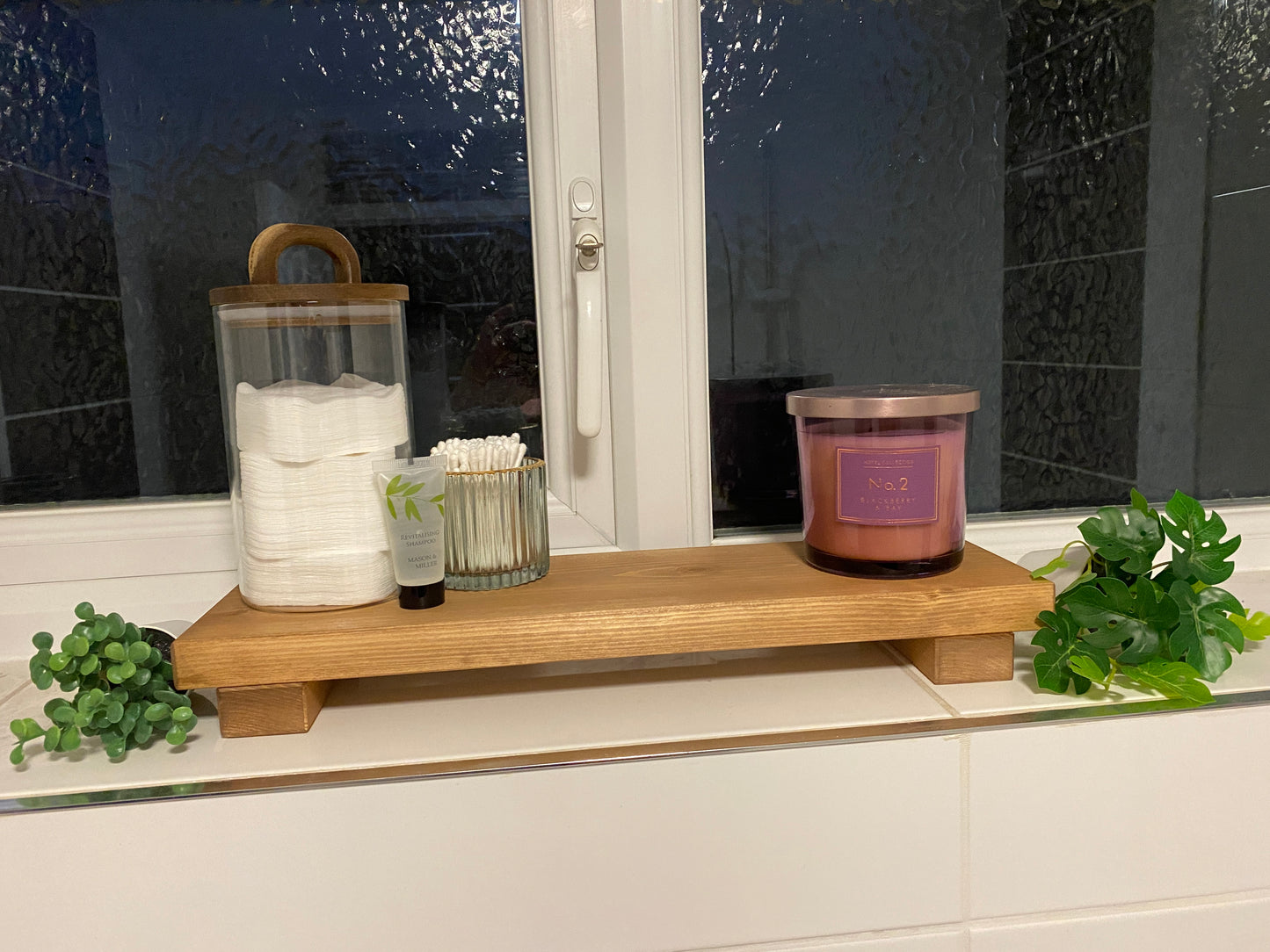 A wooden shelf that stands on two flat wooden legs. It is ideal for placing items on like bottles or candles.
