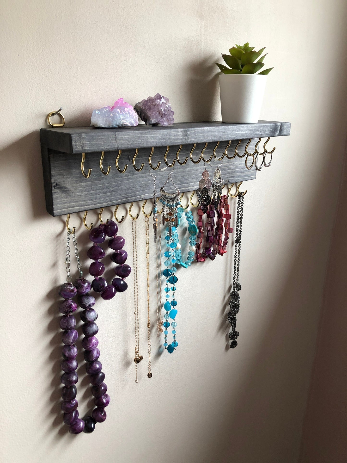 Wall-mounted jewellery organiser with 30 hooks, available in various colours including Woodland and Rustic Oak. Handcrafted from carefully selected timber, each piece boasts unique natural grain patterns. Customize with brass or upgrade to silver/chrome hooks and D rings