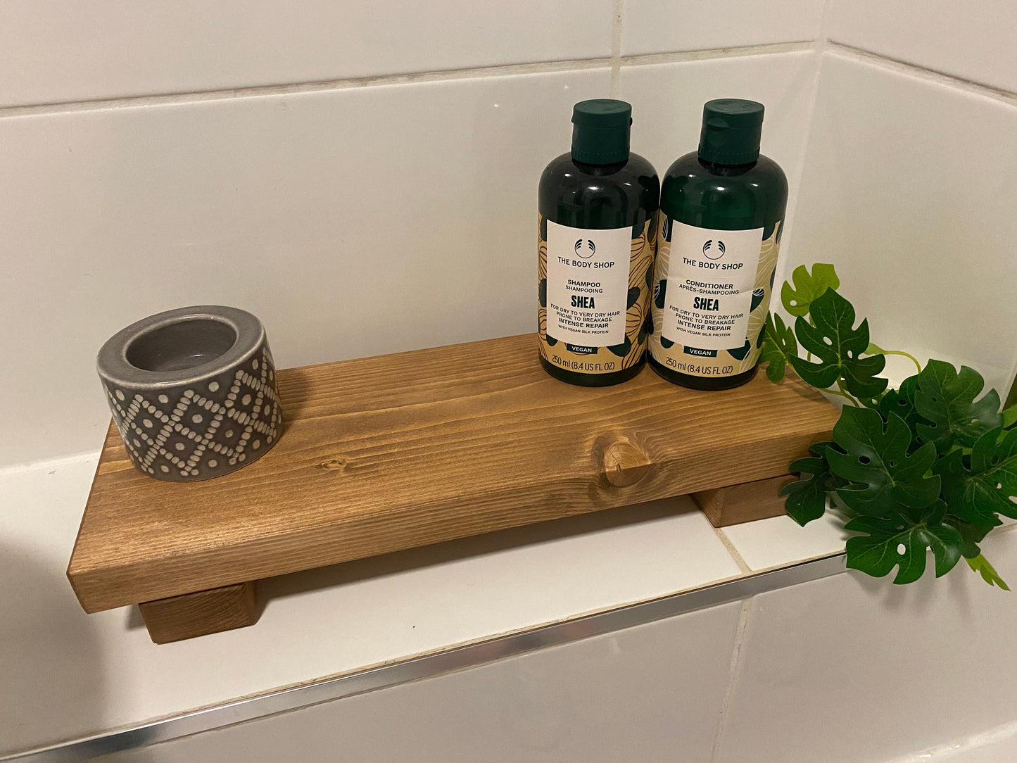 A wooden shelf that stands on two flat wooden legs. It is ideal for placing items on like bottles or candles.