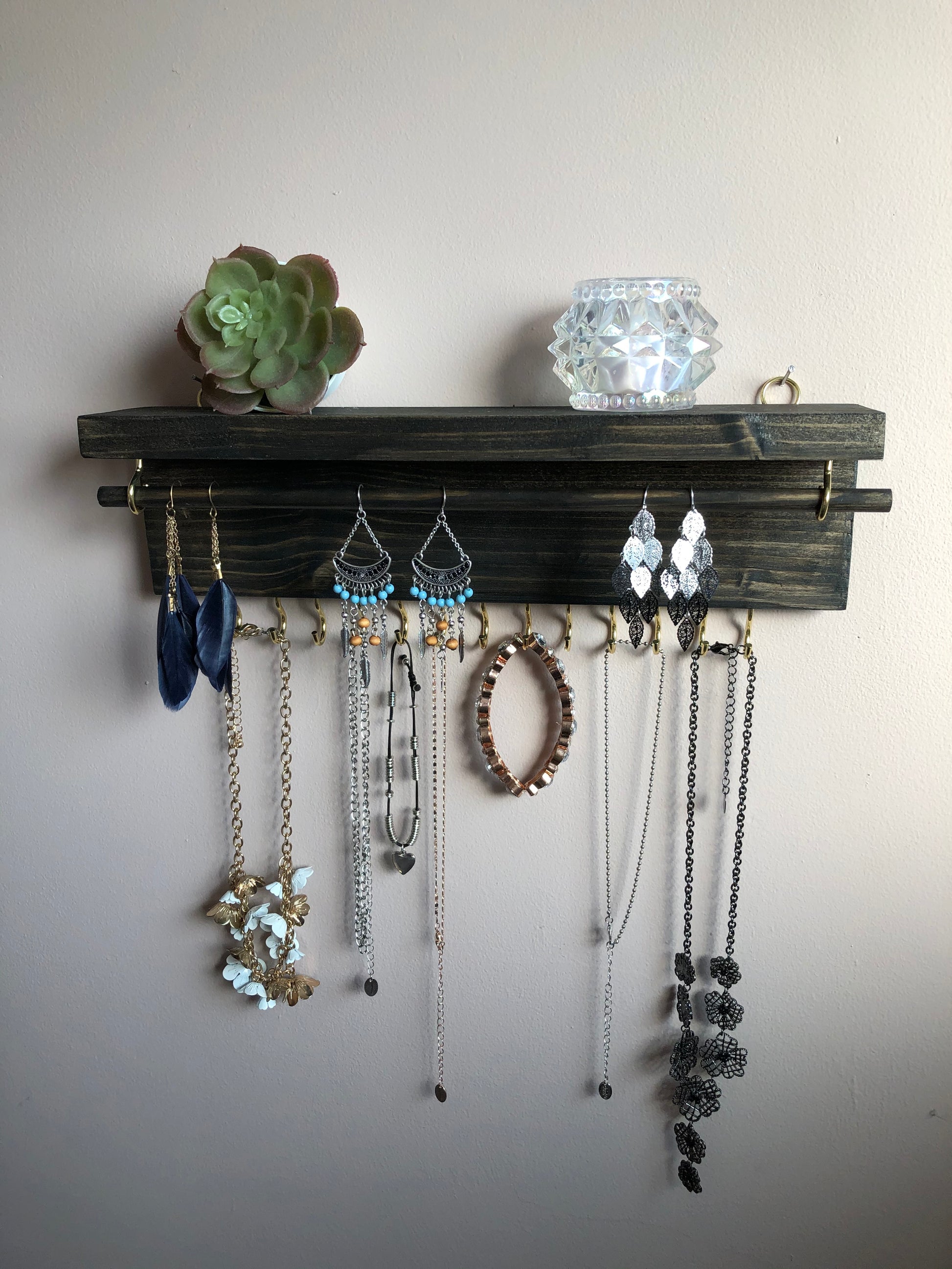  Handmade Wooden Jewellery Organiser and Earring Display featuring 13 brass hooks and a 9mm wooden dowel for versatile storage. Sleek Dark Walnut stain enhances its timeless elegance. Customize with brass or upgrade to silver/chrome hooks and D rings. Accessorize your decor effortlessly.