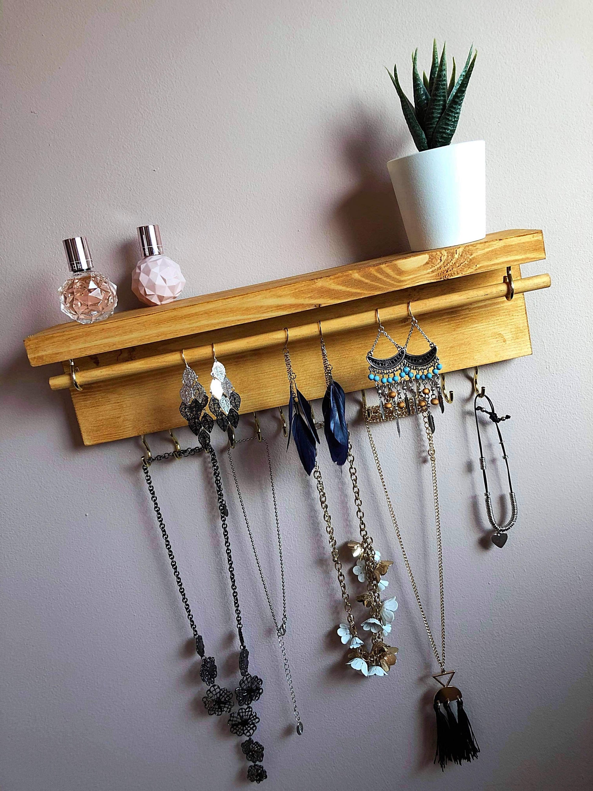 Handmade Wooden Jewellery Organiser and Earring Display featuring 13 brass hooks and a 9mm wooden dowel for versatile storage. Sleek Dark Walnut stain enhances its timeless elegance. Customize with brass or upgrade to silver/chrome hooks and D rings. Accessorize your decor effortlessly.