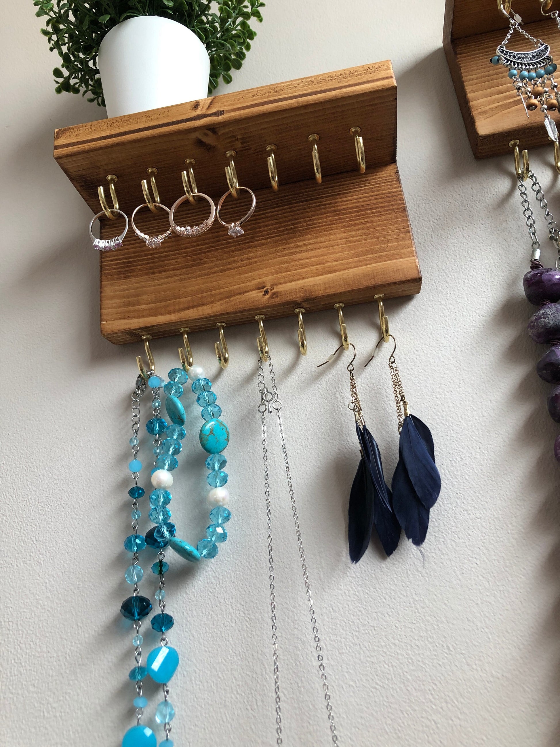 Each organizer, measuring 16cm in length, provides compact storage adaptable to any wall space, boasting a total of 28 hooks for ample room to elegantly display your favorite pieces. Featuring convenient D rings for easy hanging, these organizers double as additional shelving, perfect for storing smaller accessories. Handcrafted from carefully selected timber, each piece exudes natural charm with unique grain patterns, available in enchanting colors like Woodland, Rustic Oak, and Ebony.