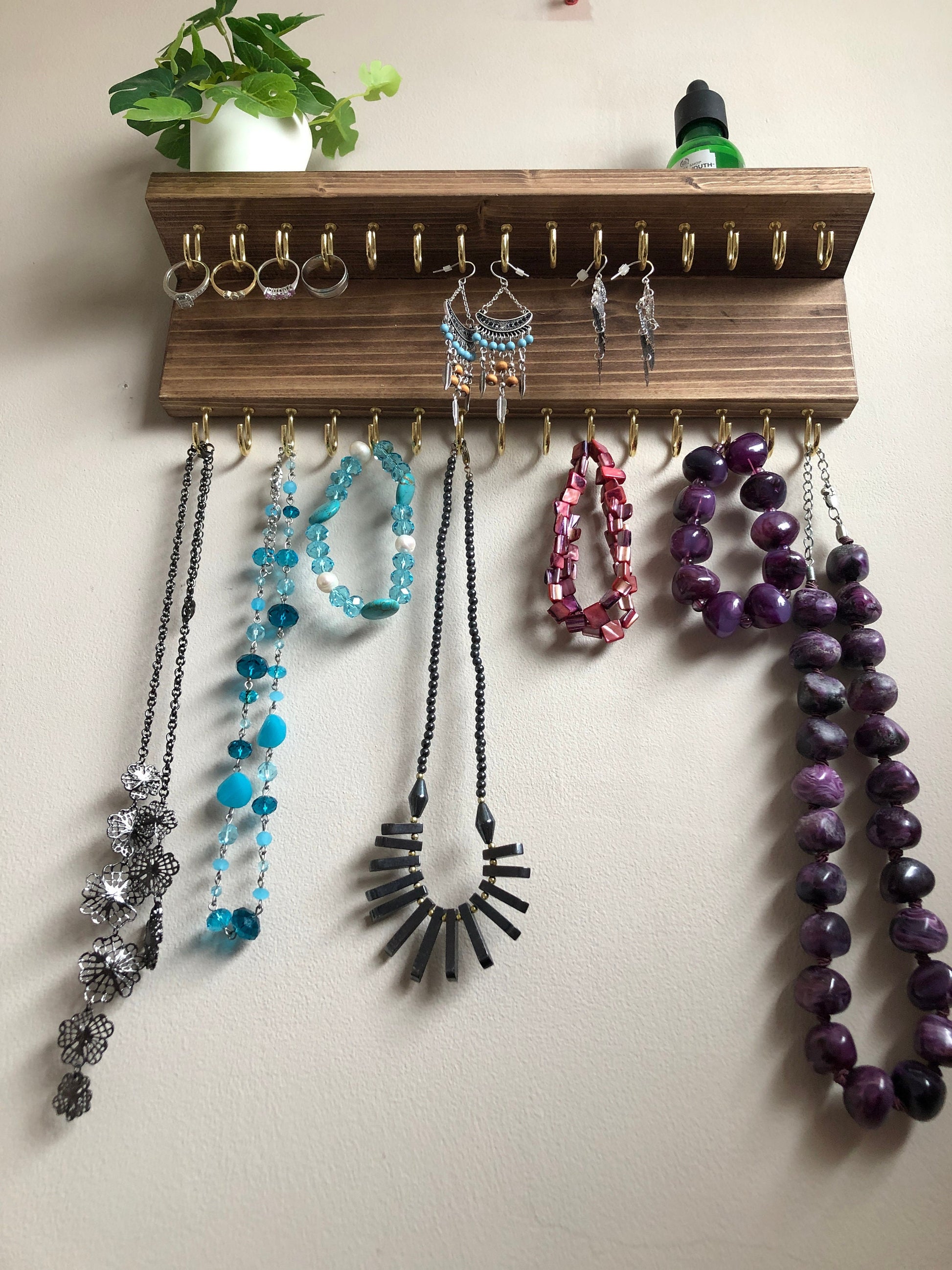 Wall-mounted jewellery organiser with 30 hooks, available in various colours including Woodland and Rustic Oak. Handcrafted from carefully selected timber, each piece boasts unique natural grain patterns. Customize with brass or upgrade to silver/chrome hooks and D rings