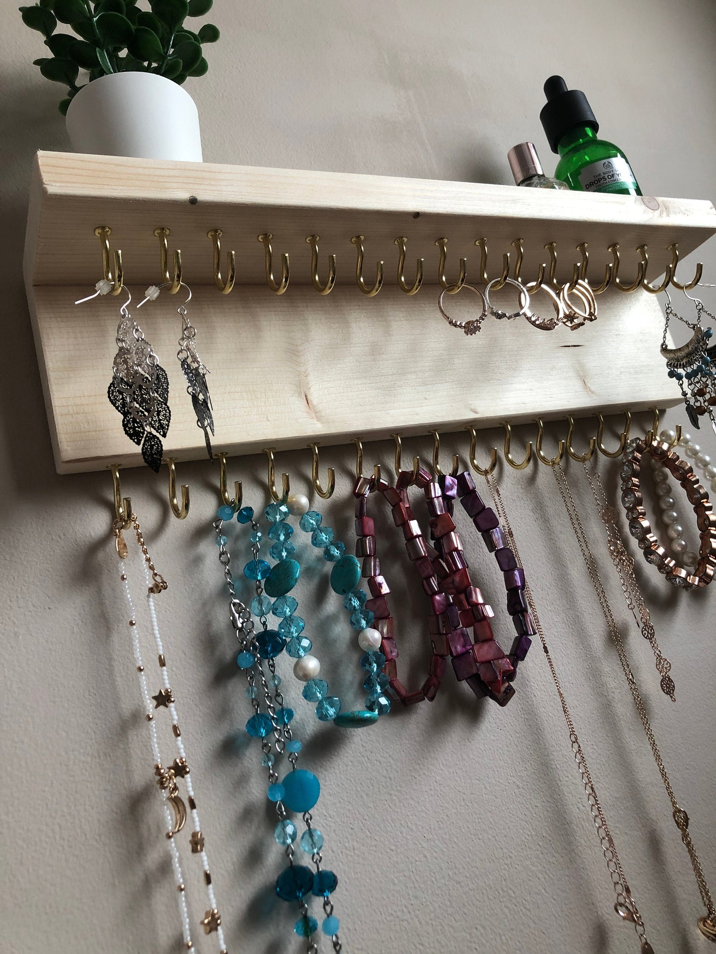 Wall-mounted jewellery organiser with 30 hooks, available in various colours including Woodland and Rustic Oak. Handcrafted from carefully selected timber, each piece boasts unique natural grain patterns. Customize with brass or upgrade to silver/chrome hooks and D rings