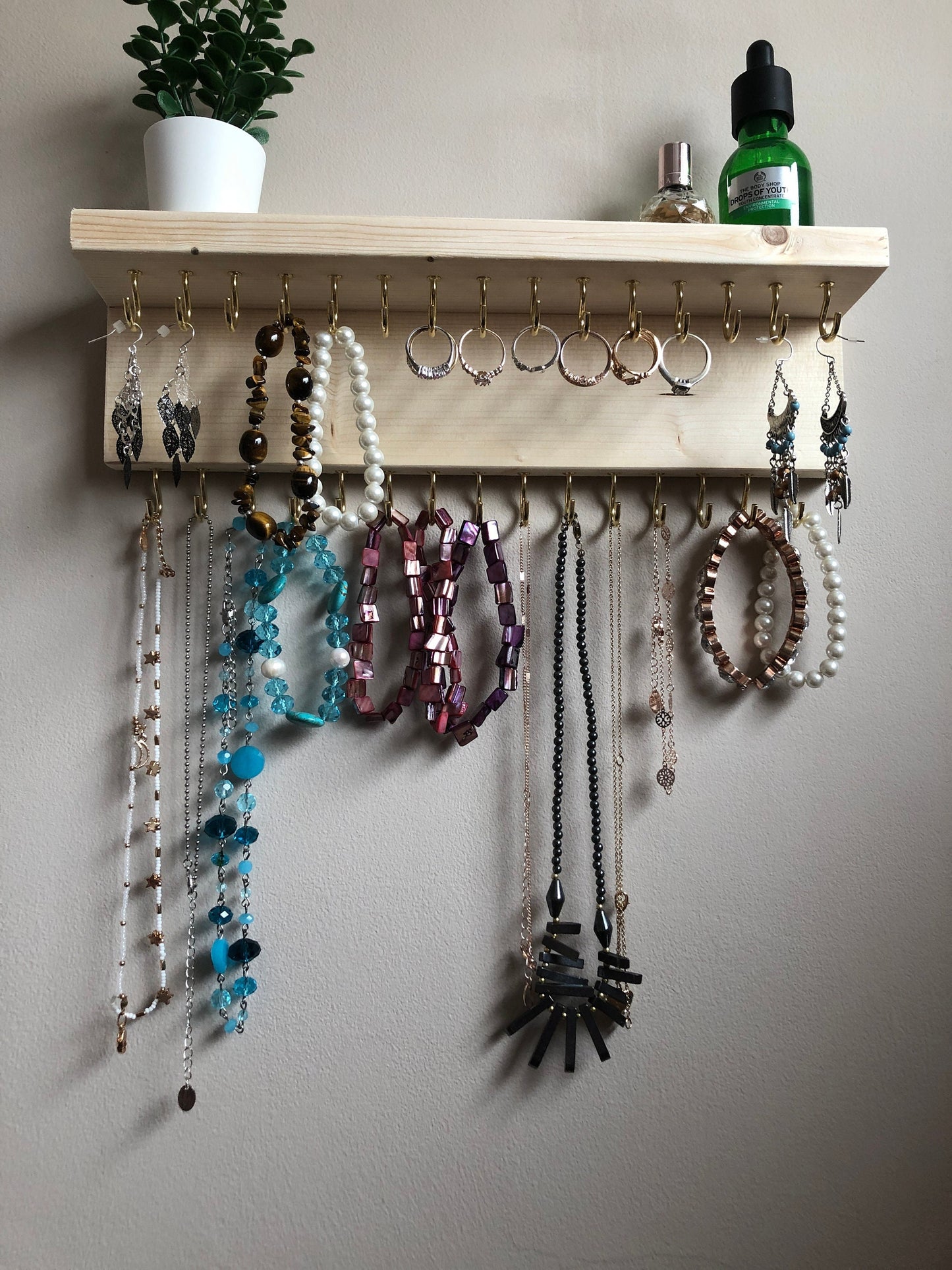 Wall-mounted jewellery organiser with 30 hooks, available in various colours including Woodland and Rustic Oak. Handcrafted from carefully selected timber, each piece boasts unique natural grain patterns. Customize with brass or upgrade to silver/chrome hooks and D rings