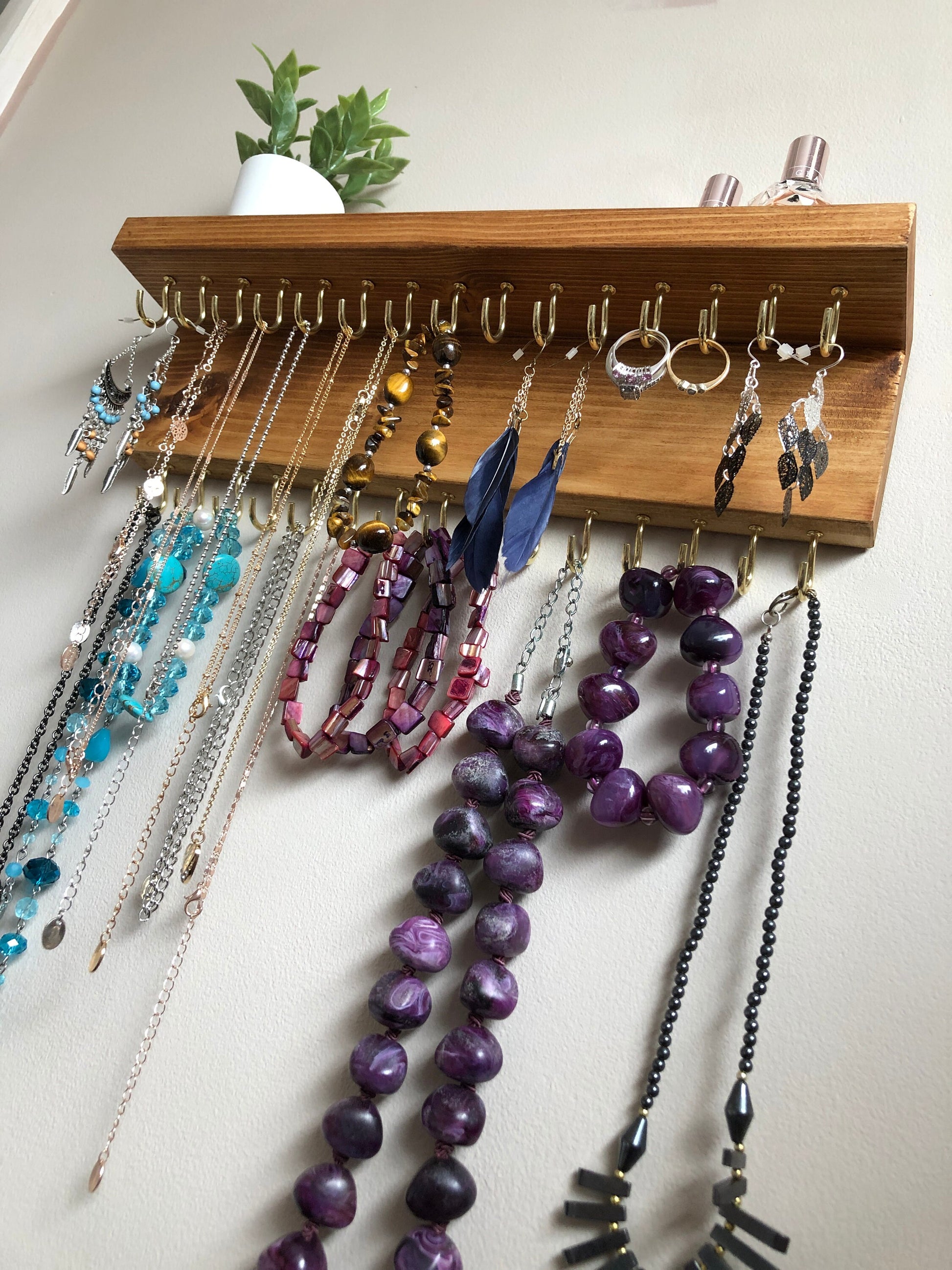 Wall-mounted jewellery organiser with 30 hooks, available in various colours including Woodland and Rustic Oak. Handcrafted from carefully selected timber, each piece boasts unique natural grain patterns. Customize with brass or upgrade to silver/chrome hooks and D rings