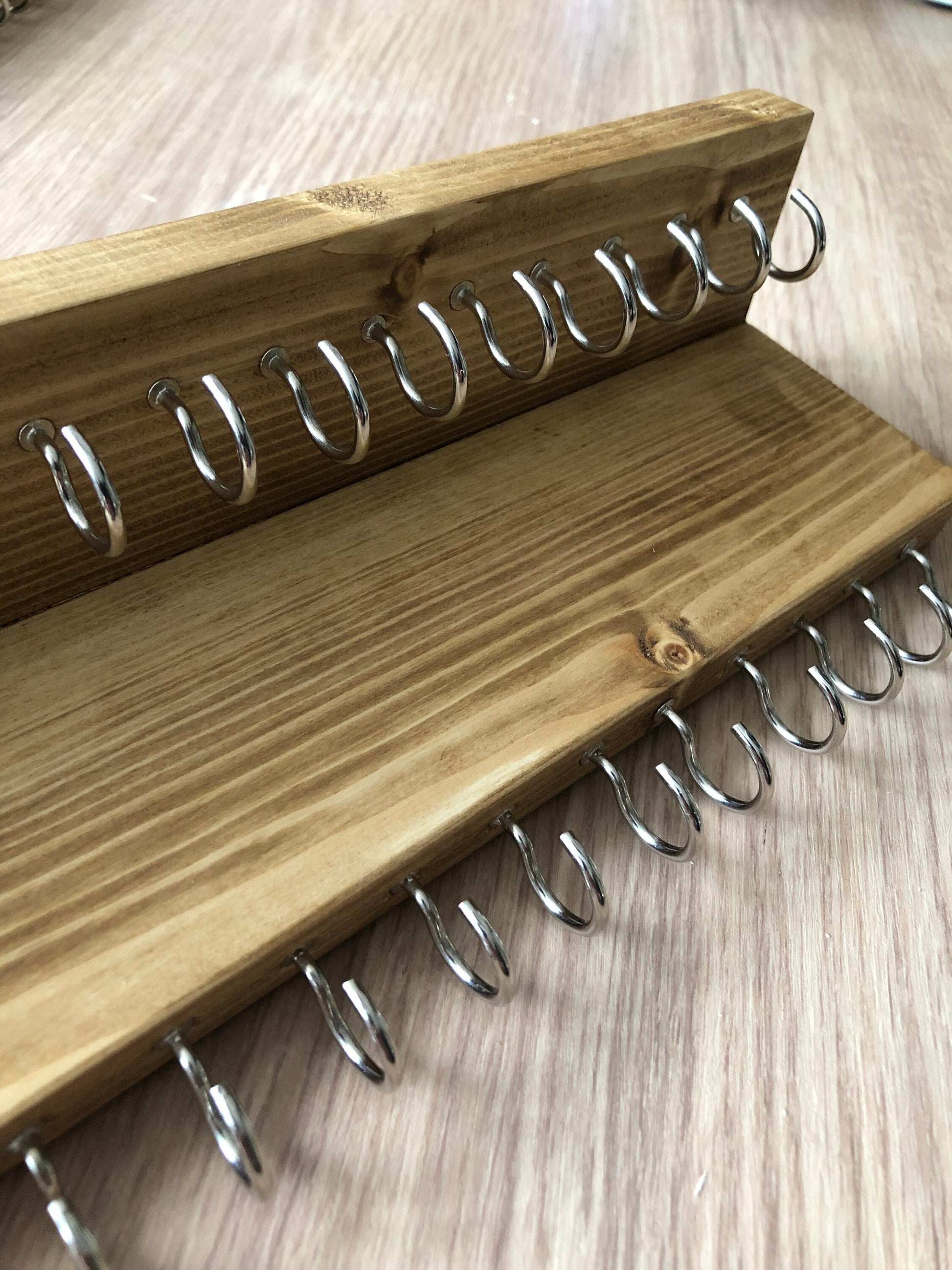 Wall-mounted jewellery organiser with 30 hooks, available in various colours including Woodland and Rustic Oak. Handcrafted from carefully selected timber, each piece boasts unique natural grain patterns. Customize with brass or upgrade to silver/chrome hooks and D rings