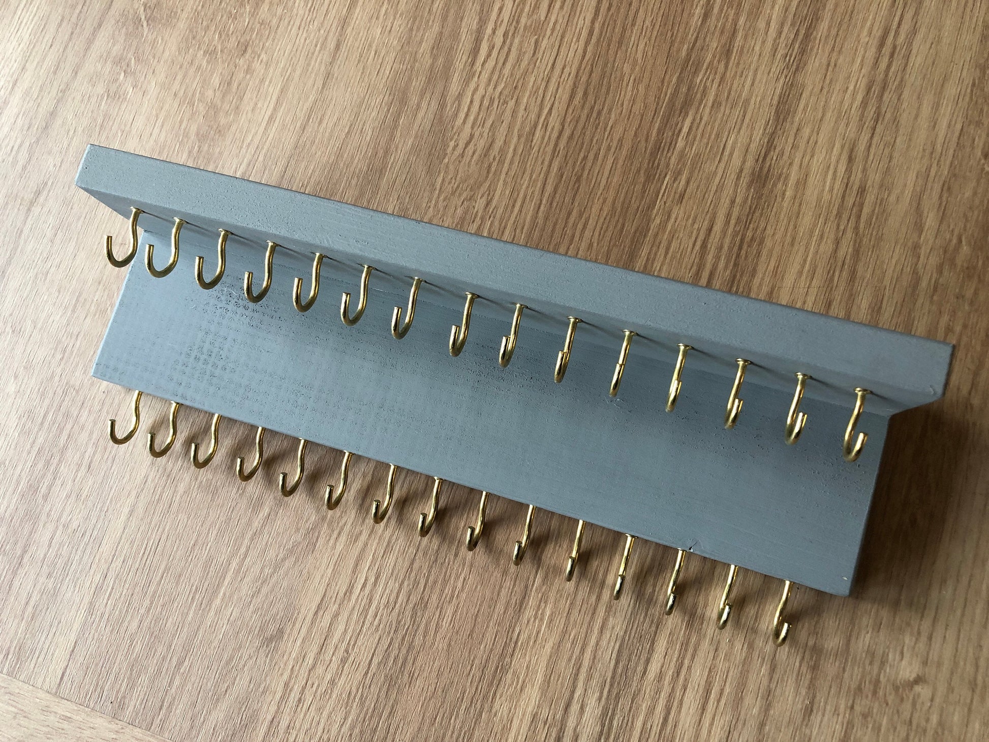 Small style shelf jewellery organiser with two rows of hooks for necklace and jewellry storage. Bottom row of hooks visible beneath the shelf, while another row is discreetly tucked underneath the top ledge. Ideal for keeping your accessories neatly organised and easily accessible.