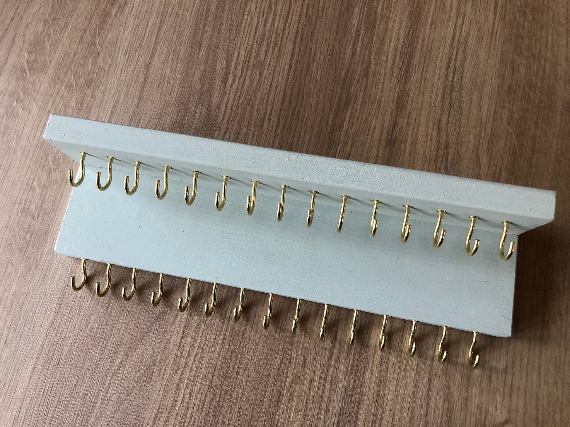 Small style shelf jewellery organiser with two rows of hooks for necklace and jewellry storage. Bottom row of hooks visible beneath the shelf, while another row is discreetly tucked underneath the top ledge. Ideal for keeping your accessories neatly organised and easily accessible.