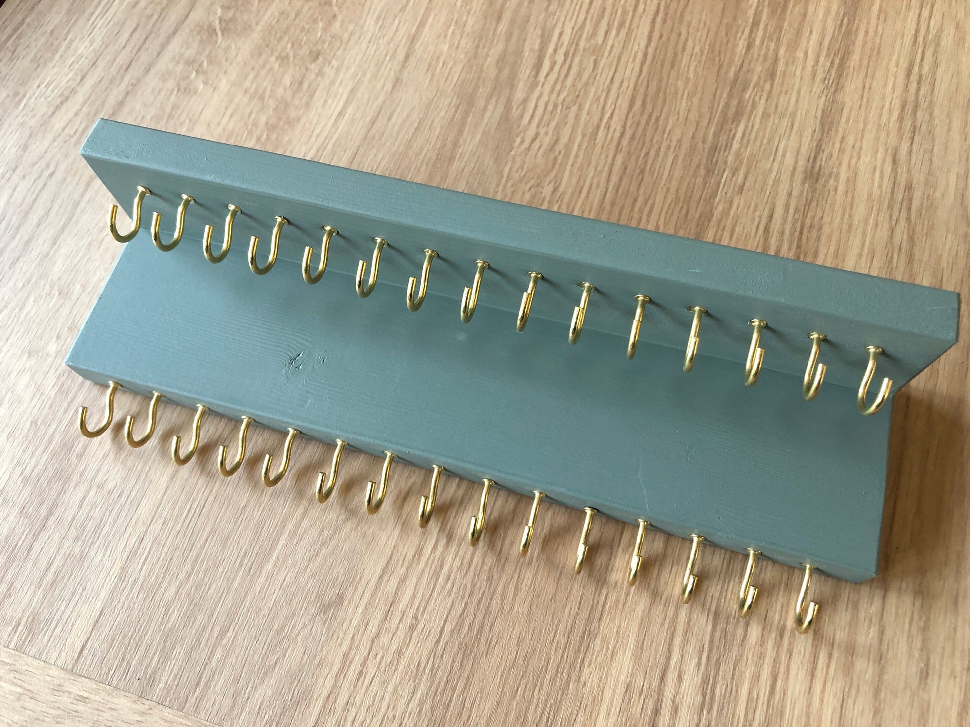 Small style shelf jewellery organiser with two rows of hooks for necklace and jewellry storage. Bottom row of hooks visible beneath the shelf, while another row is discreetly tucked underneath the top ledge. Ideal for keeping your accessories neatly organised and easily accessible.