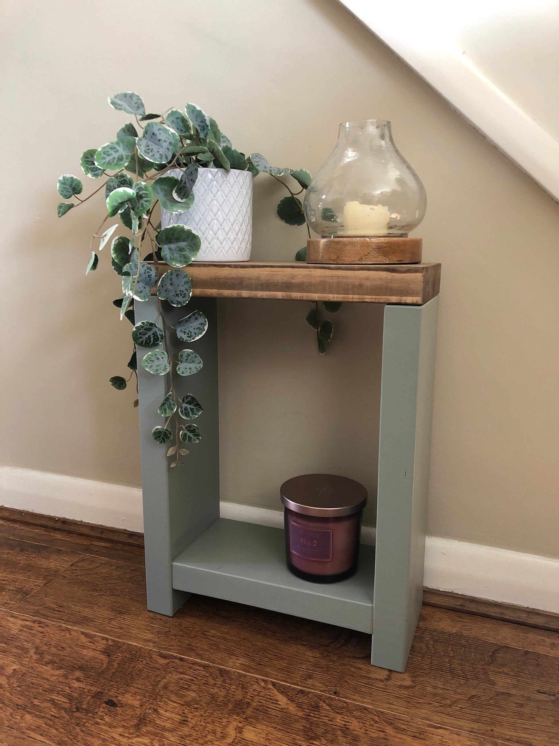 Handmade narrow side table crafted from carefully selected timber, versatile for various settings Features spacious top for plants or candles and low shelf for books or tall vase. Finished with two-tone effect: base in select Farrow and Ball colors, top in Dark Oak or Medium Oak wood dye. Dimensions: H: 44.5cm, W: 33cm, D: 14cm, with 33cm height between shelf and top. Enjoy FREE delivery on all handmade items. Order now for a carefully packaged product crafted with love. Build time: 3-4 weeks.