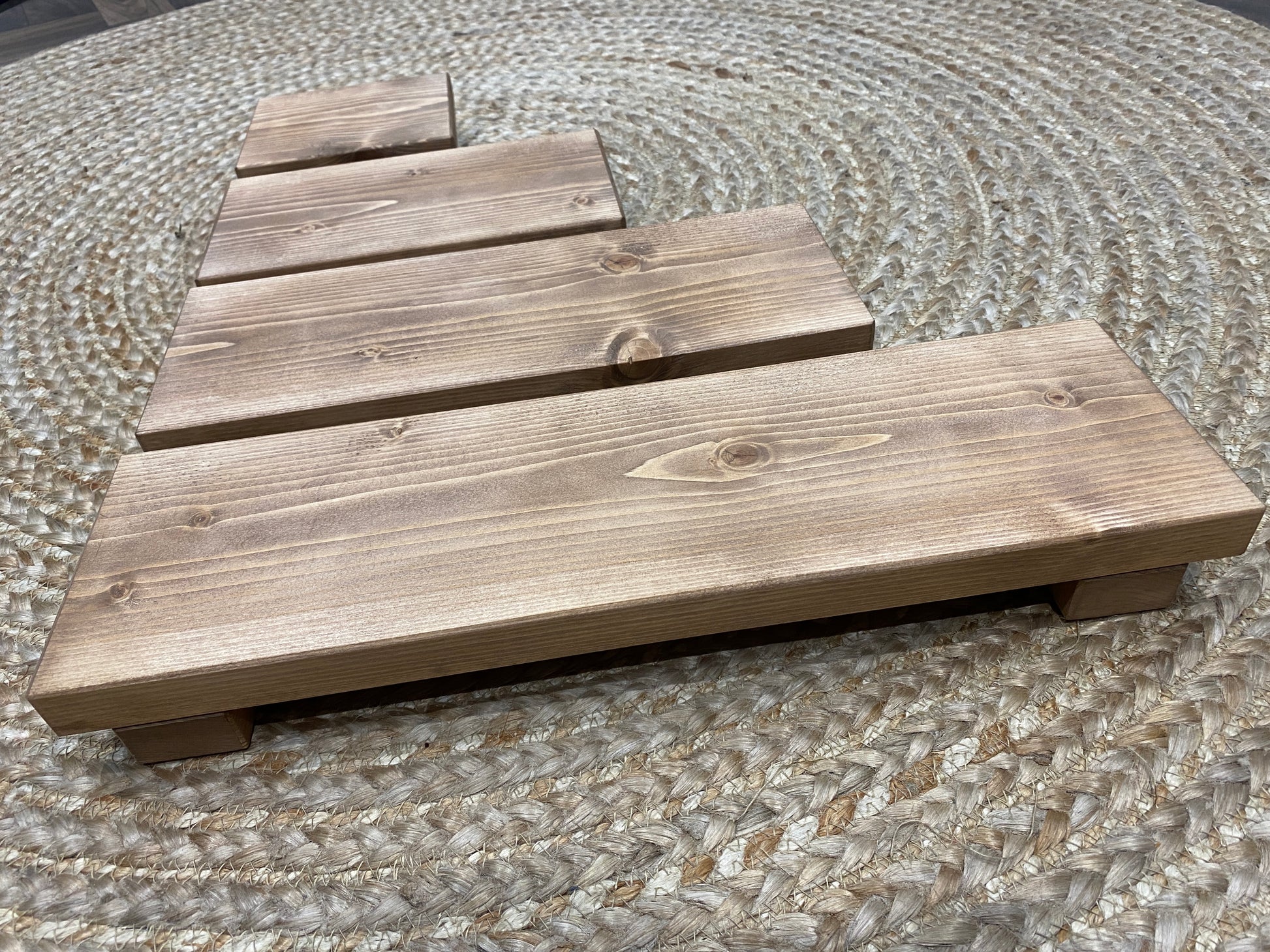 A wooden shelf that stands on two flat wooden legs. It is ideal for placing items on like bottles or candles.