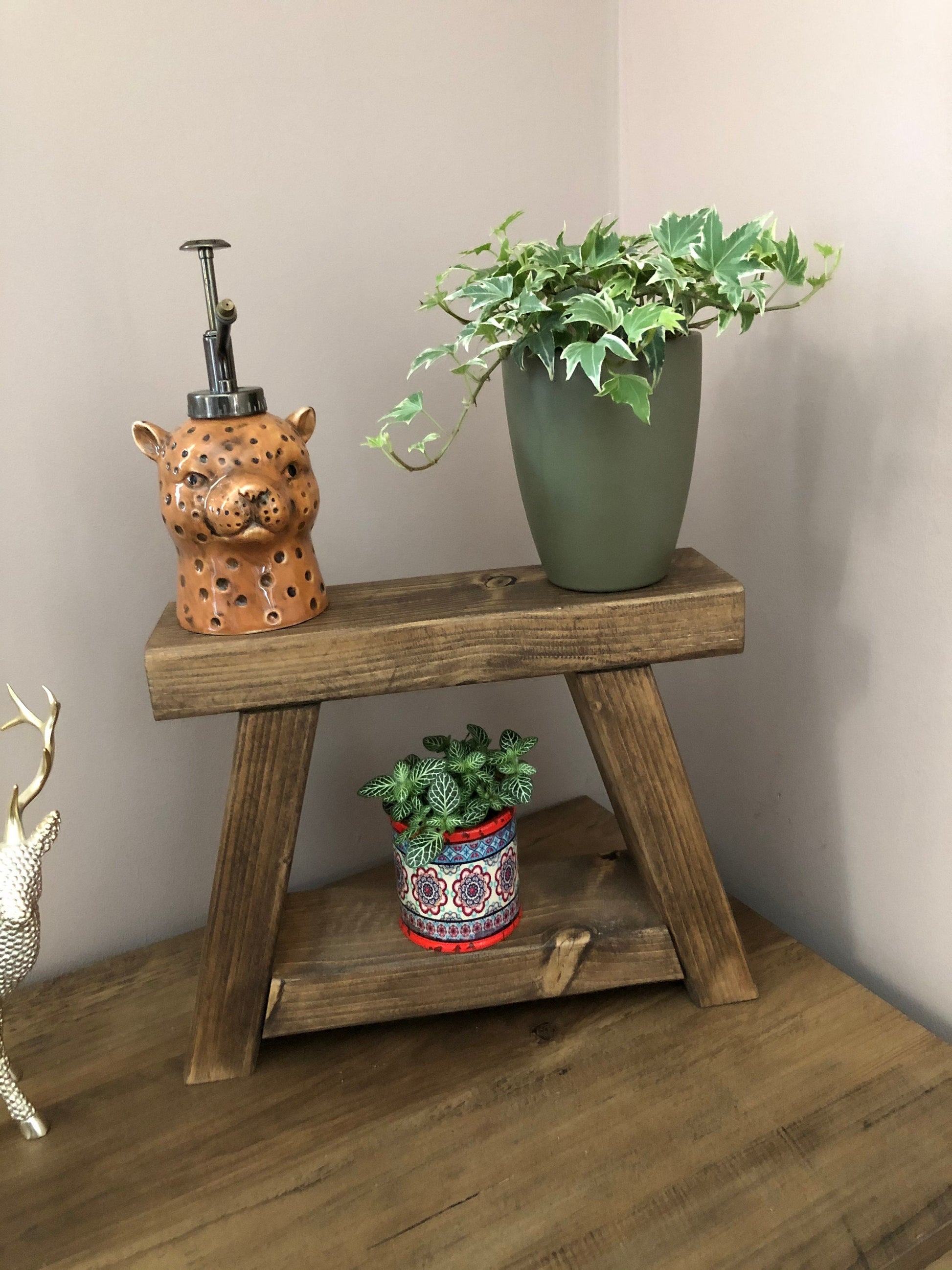 Handmade small rustic-style display stool with chunky shelves, perfect for living rooms, kitchens, and bathrooms. Ideal for house plants, beauty products, cosmetics, and candles. Made to order with options of Rustic Oak, Fir Cone, or Plain Untreated finish. Measurements: Total Height 10 inches, Width 11.75 inches, Depth 3.5 inches. Crafted with care, ensuring each piece is inspected for beauty and quality.