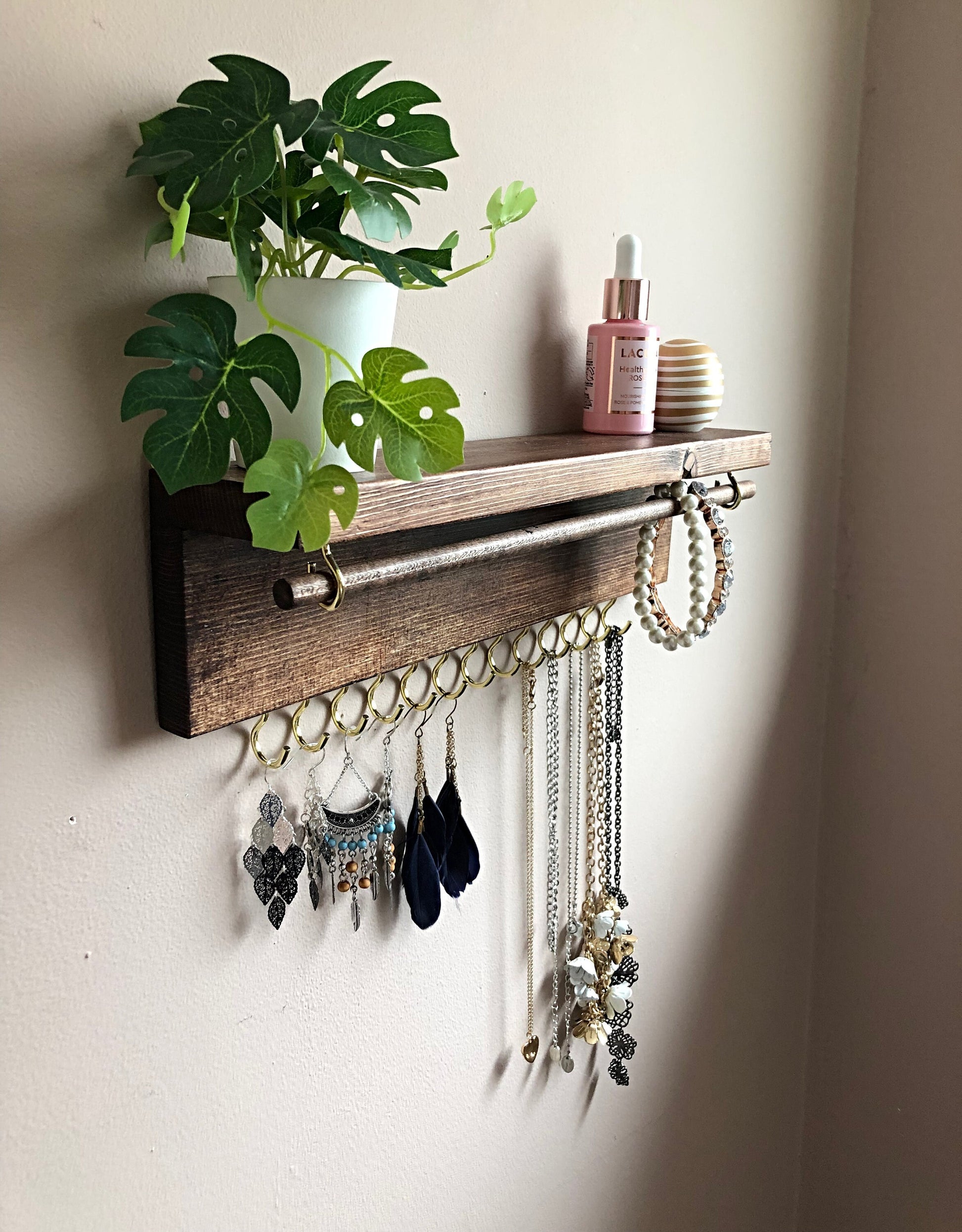  Handmade Wooden Jewellery Organiser and Earring Display featuring 13 brass hooks and a 9mm wooden dowel for versatile storage. Sleek Dark Walnut stain enhances its timeless elegance. Customize with brass or upgrade to silver/chrome hooks and D rings. Accessorize your decor effortlessly.