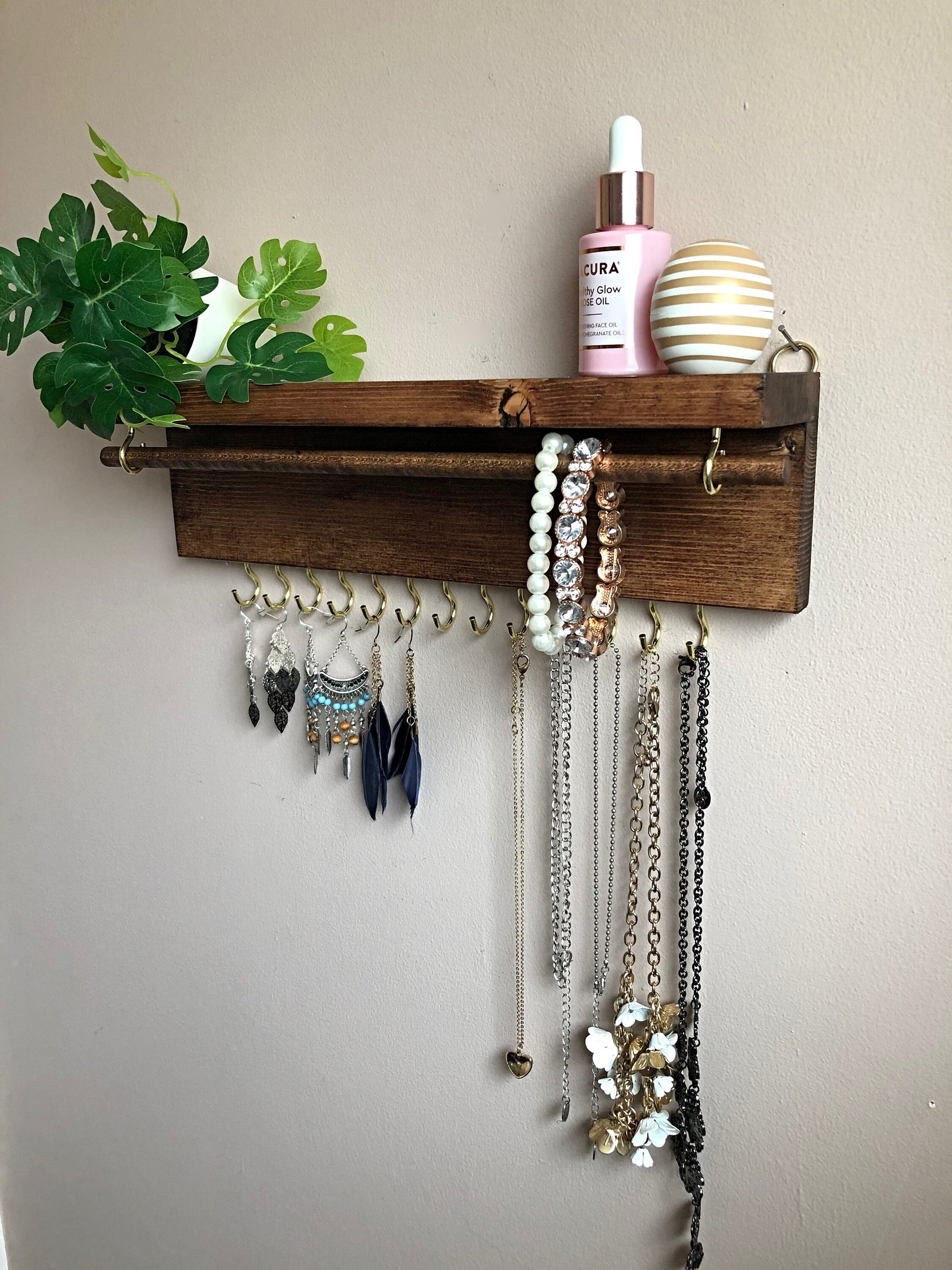  Handmade Wooden Jewellery Organiser and Earring Display featuring 13 brass hooks and a 9mm wooden dowel for versatile storage. Sleek Dark Walnut stain enhances its timeless elegance. Customize with brass or upgrade to silver/chrome hooks and D rings. Accessorize your decor effortlessly.