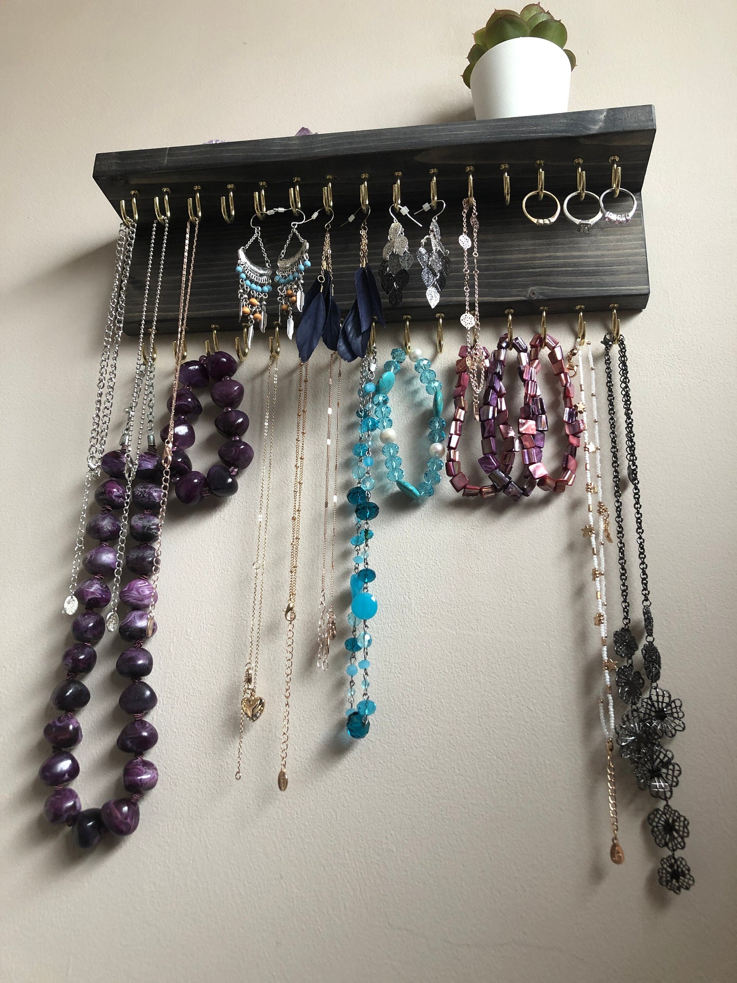 Wall-mounted jewellery organiser with 30 hooks, available in various colours including Woodland and Rustic Oak. Handcrafted from carefully selected timber, each piece boasts unique natural grain patterns. Customize with brass or upgrade to silver/chrome hooks and D rings