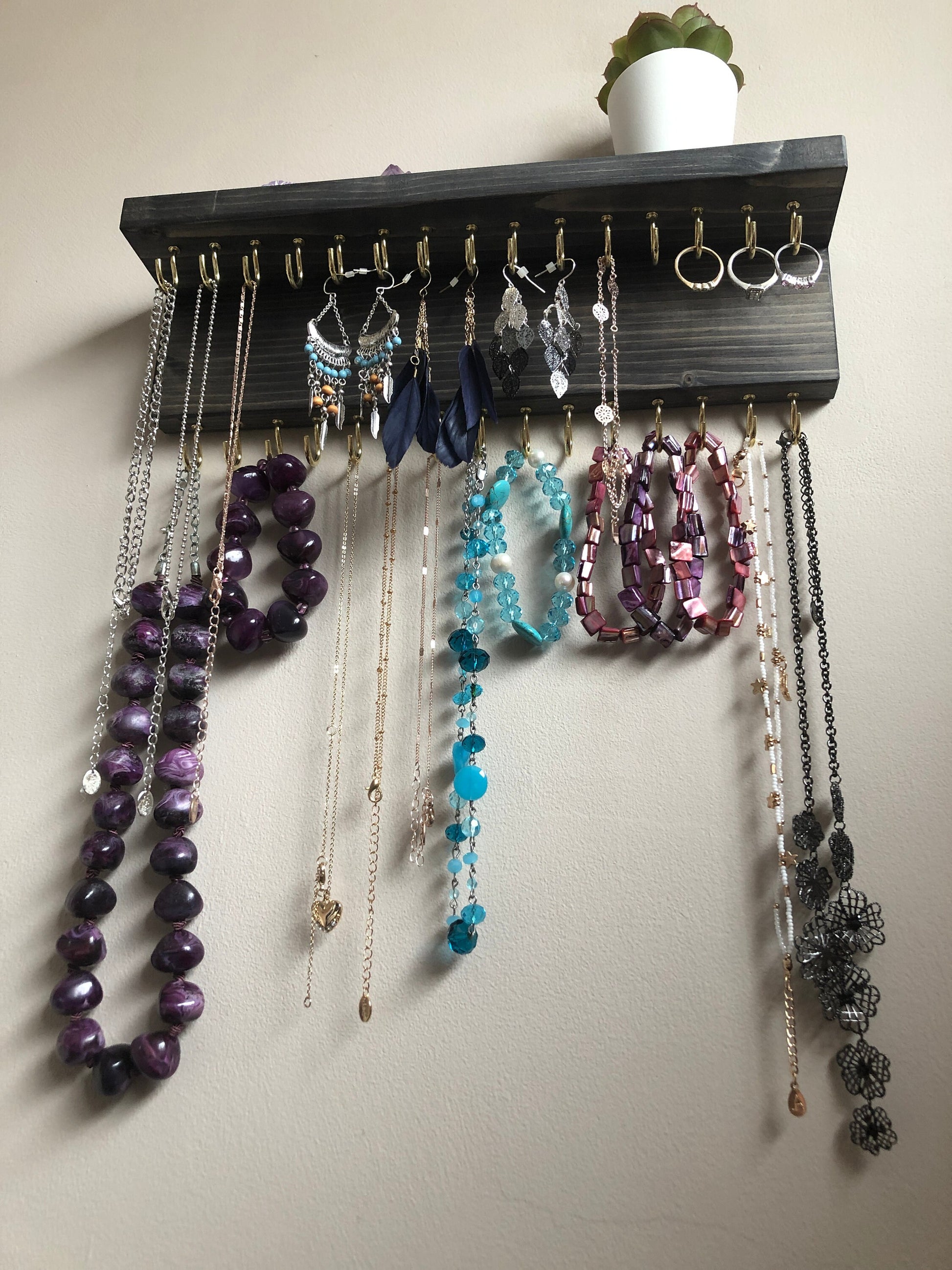 Wall-mounted jewellery organiser with 30 hooks, available in various colours including Woodland and Rustic Oak. Handcrafted from carefully selected timber, each piece boasts unique natural grain patterns. Customize with brass or upgrade to silver/chrome hooks and D rings